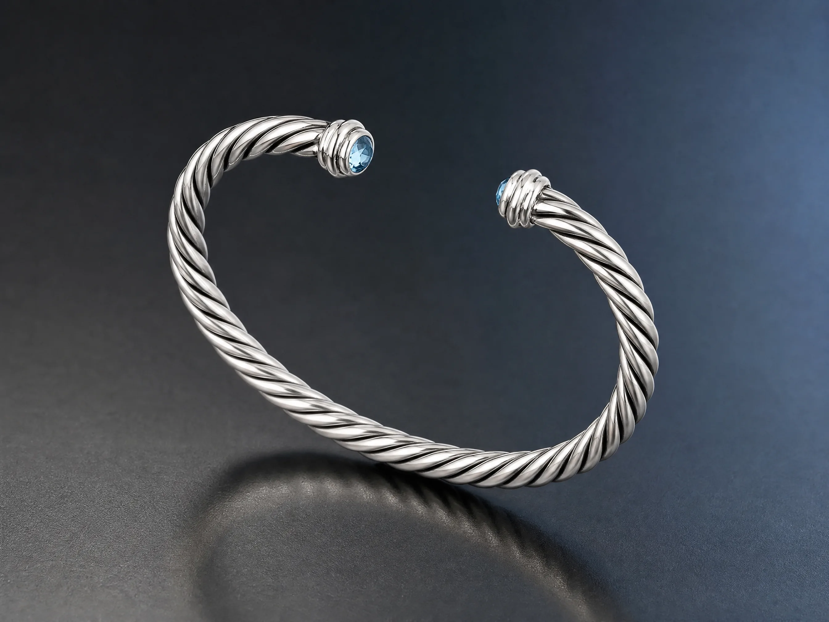 A silver cable bracelet with blue stone details in controlled jewelry lighting.